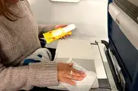 a person using a Wet Ones Antibacterial Hand Wipe to clean the tray table on a plane
