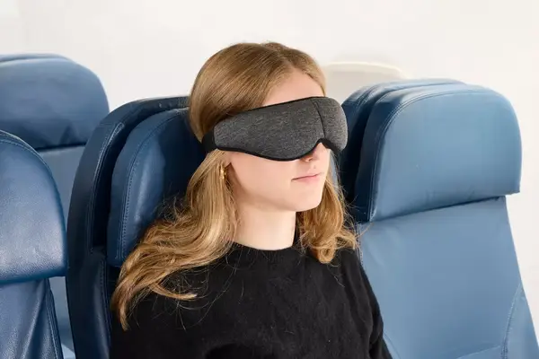 A person wearing the Ostrichpillow Ergonomic Eye Mask on an airplane