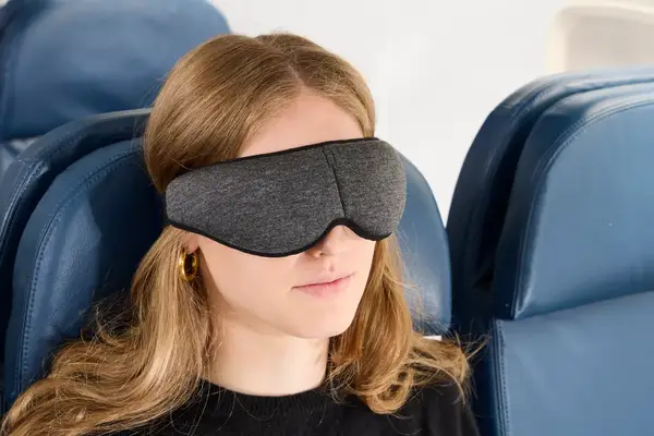 Close up of a person wearing the Ostrichpillow Ergonomic Eye Mask on an airplane