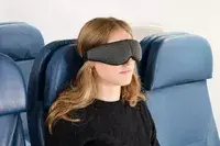 A person wearing the Ostrichpillow Ergonomic Eye Mask on an airplane