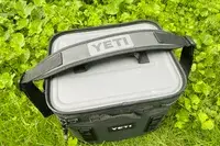 A Yeti Hopper Flip 12 Soft Cooler sits outdoors in foliage