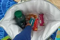 A person reaches for a canned drink inside the Calpak Insulated Soft-sided Cooler