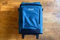 The Coleman Chiller 42-Can Soft-Sided Portable Cooler with Wheels on a wooden floor