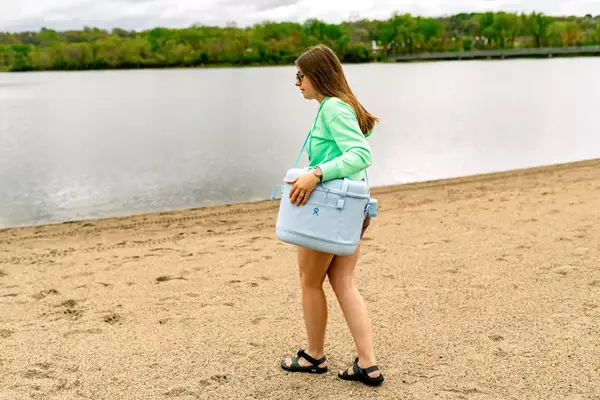 A person carries the Hydro Flask 20L Carry Out Soft Cooler Travel Bag on a beach
