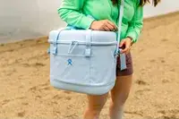 A person carries the Hydro Flask 20L Carry Out Soft Cooler Travel Bag by the shoulder strap