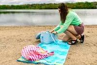 A person unpacks the Hydro Flask 20L Carry Out Soft Cooler Travel Bag on a beach