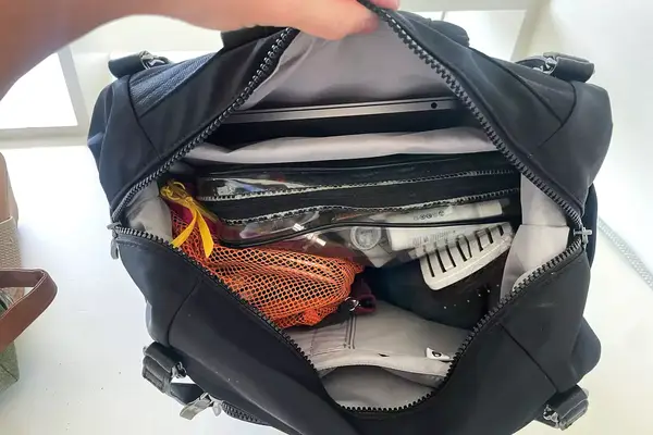 A person holds the Baggallini Nolita Convertible Backpack open to show the items inside