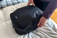 Two hands holding a Patagonia Black Hole Cube, Large 14L on a bed