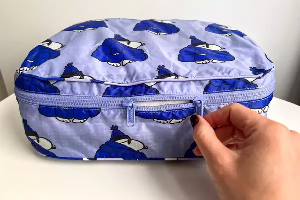 A hand holding a zipper of the Baggu Packing Cube Set