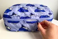 A hand holding a zipper of the Baggu Packing Cube Set