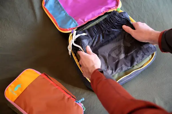 Two hands packing a Cotopaxi Cubos Packing Cube