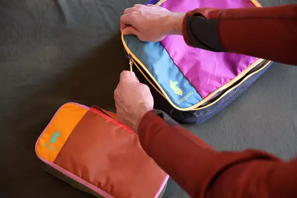 Two hands zippering closed a Cotopaxi Cubos Packing Cube