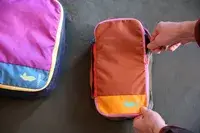 Two hands closing a Cotopaxi Cubos Packing Cube