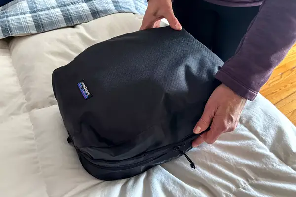 Two hands holding a Patagonia Black Hole Cube, Large 14L on a bed