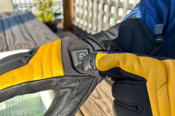 A person presses the power button on the Gobi Heat ​​Vertex II Heated Ski Gloves