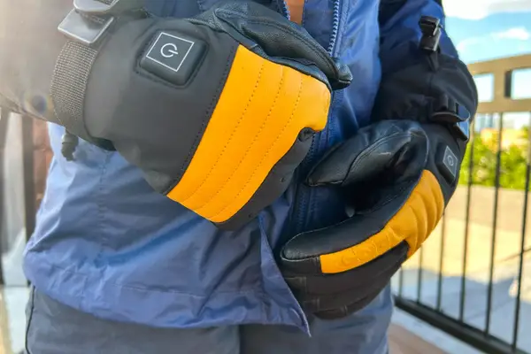A person zips up a jacket while wearing the Gobi Heat ​​Vertex II Heated Ski Gloves