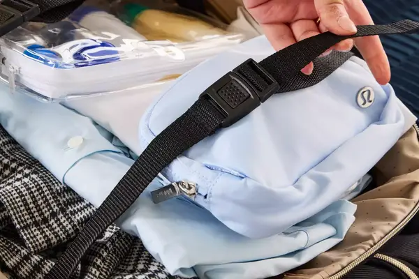 A person touches the strap on the Kenneth Cole Reaction Chelsea Luggage Expandable Underseater Spinner