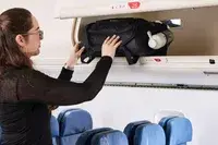 A person places the Rockland Melrose Upright Wheeled Underseater Luggage into an overhead compartment