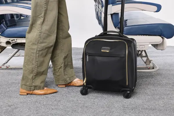 A person wheels the Tumi Voyageur Léger Compact Carry-on over carpet