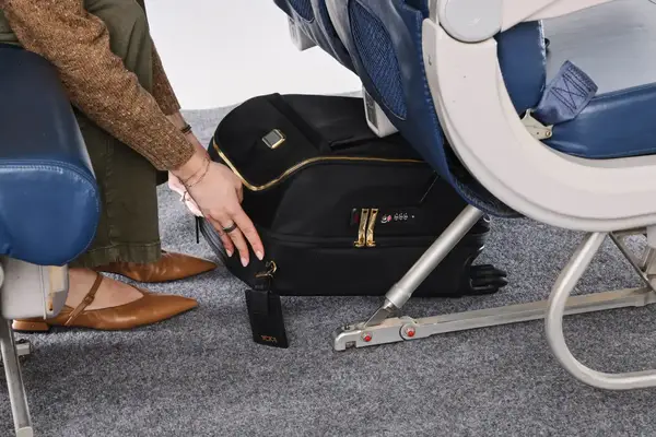 A person places the Tumi Voyageur Léger Compact Carry-on under an airplane seat