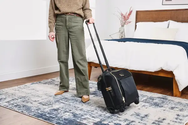 A person wheels the Tumi Voyageur Léger Compact Carry-on over a rug