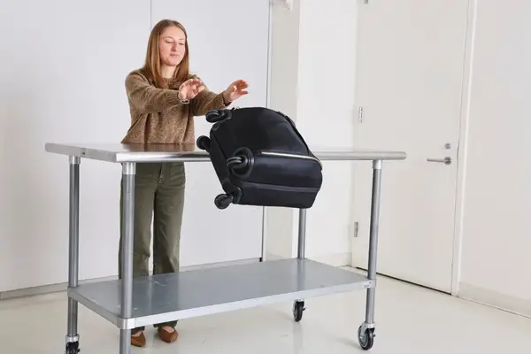 A person throws the Tumi Voyageur Léger Compact Carry-on from a metal table