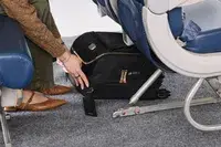 A person places the Tumi Voyageur Léger Compact Carry-on under an airplane seat