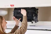 A person places the Tumi Voyageur Léger Compact Carry-on into an overhead compartment