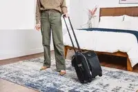 A person wheels the Tumi Voyageur Léger Compact Carry-on over a rug