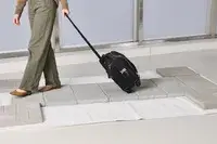 A person wheels the Tumi Voyageur Léger Compact Carry-on over paving stones