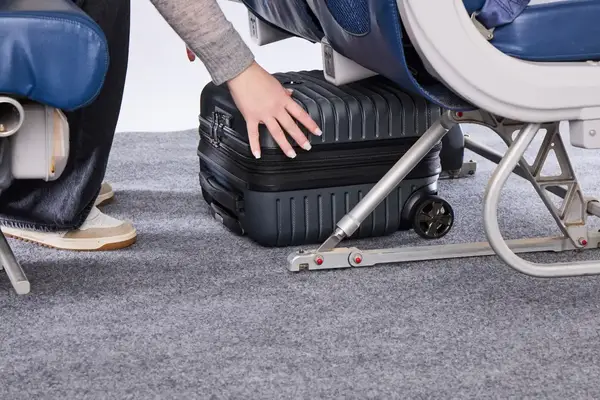 A person places the Delsey Paris Cruise 3.0 2-Wheeled Underseater under an airplane seat