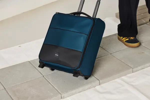 A person wheels the Antler Soft Stripe Underseat Luggage over stone pavers