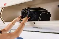 A person places the Kenneth Cole Reaction Chelsea Luggage Expandable Underseater Spinner into an overhead compartment