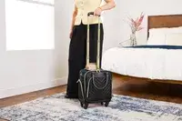 A person wheels the Kenneth Cole Reaction Chelsea Luggage Expandable Underseater Spinner over a rug