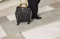 A person wheels the Kenneth Cole Reaction Chelsea Luggage Expandable Underseater Spinner over paving stones