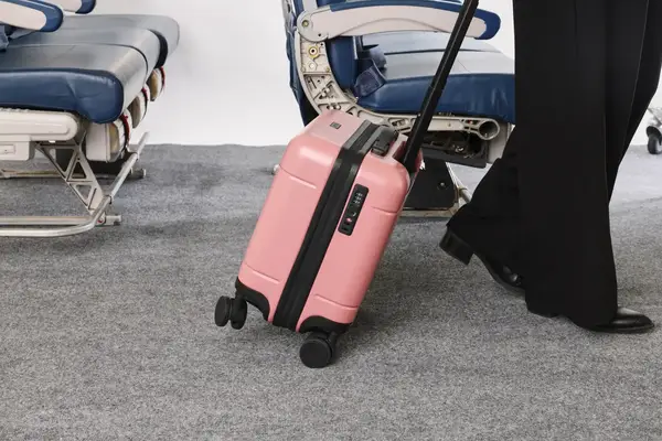 A person wheels the Calpak Hue Mini Carry-on Luggage over carpet