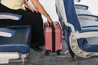 A person places the Calpak Hue Mini Carry-on Luggage under an airplane seat
