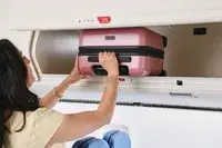 A person places the Calpak Hue Mini Carry-on Luggage into an overhead compartment