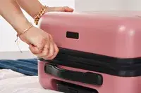 A person zips up the Calpak Hue Mini Carry-on Luggage