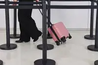 A person wheels the Calpak Hue Mini Carry-on Luggage over a linoleum floor