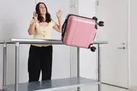 A person throws the Calpak Hue Mini Carry-on Luggage off of a metal table