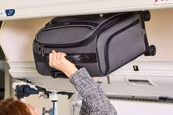 A person places the Hartmann Herringbone Deluxe Underseater into an overhead compartment
