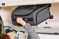 A person places the Hartmann Herringbone Deluxe Underseater into an overhead compartment