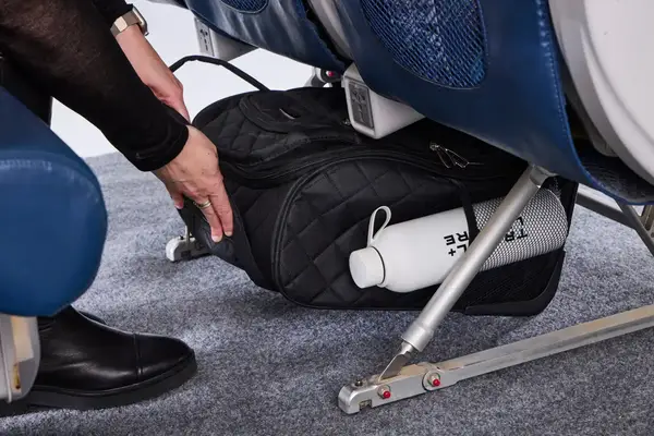 A person places the Rockland Melrose Upright Wheeled Underseater Luggage under an airplane seat