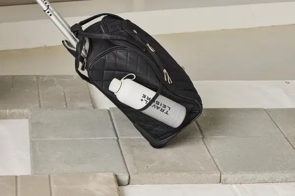 A person wheels the Rockland Melrose Upright Wheeled Underseater Luggage over paving stones