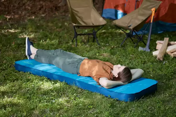 Person laying on the Therm-a-Rest MondoKing 3D Camping Sleeping Pad displayed on grass next to two camping chairs
