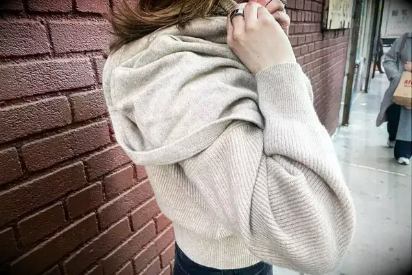 A woman putting on the hood of the Lilysilk Eshe 2-in-1 Cashmere Detachable Hoodie