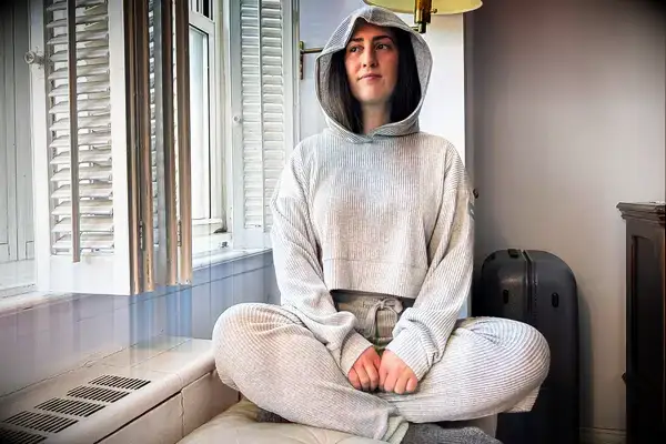A person sitting by a window wearing the Alo Muse Hoodie