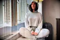 A person sitting by a window wearing the Alo Muse Hoodie