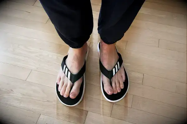 Feet wearing Adidas Comfort Flip Flops on wood floor